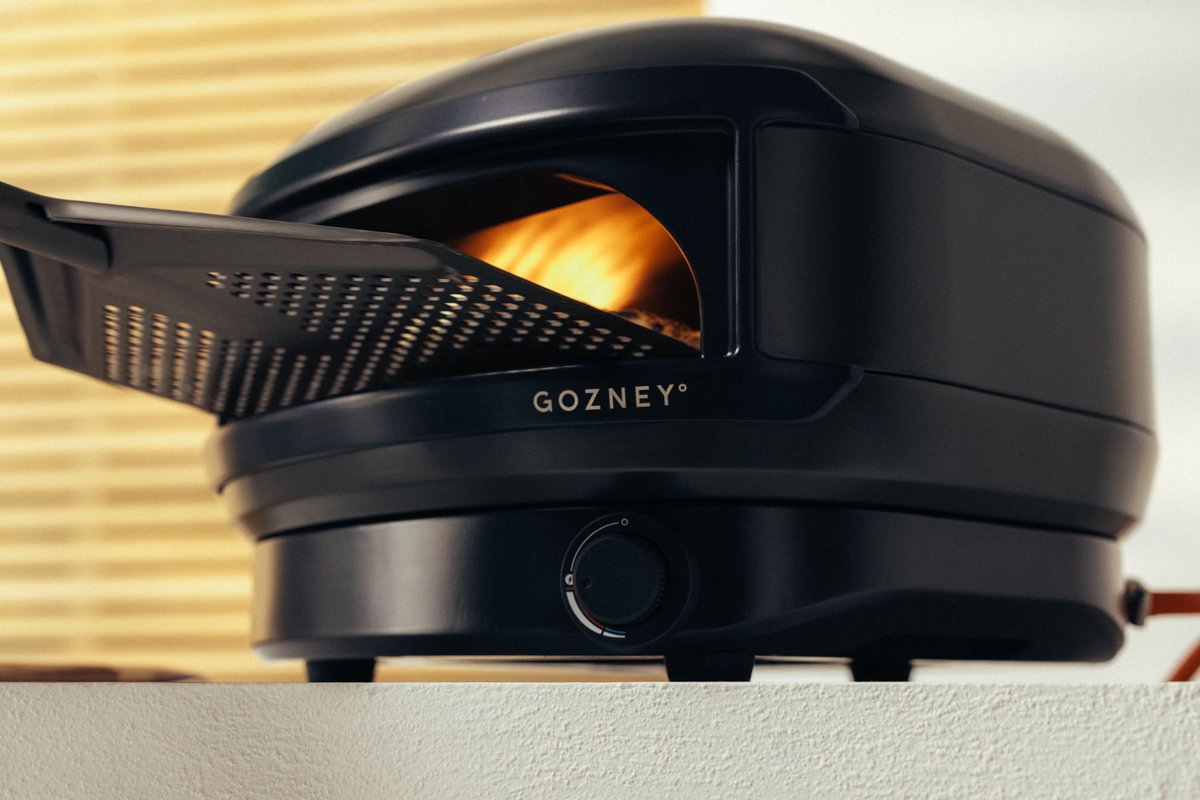 Black Gozney oven with a pizza inside on a wooden surface