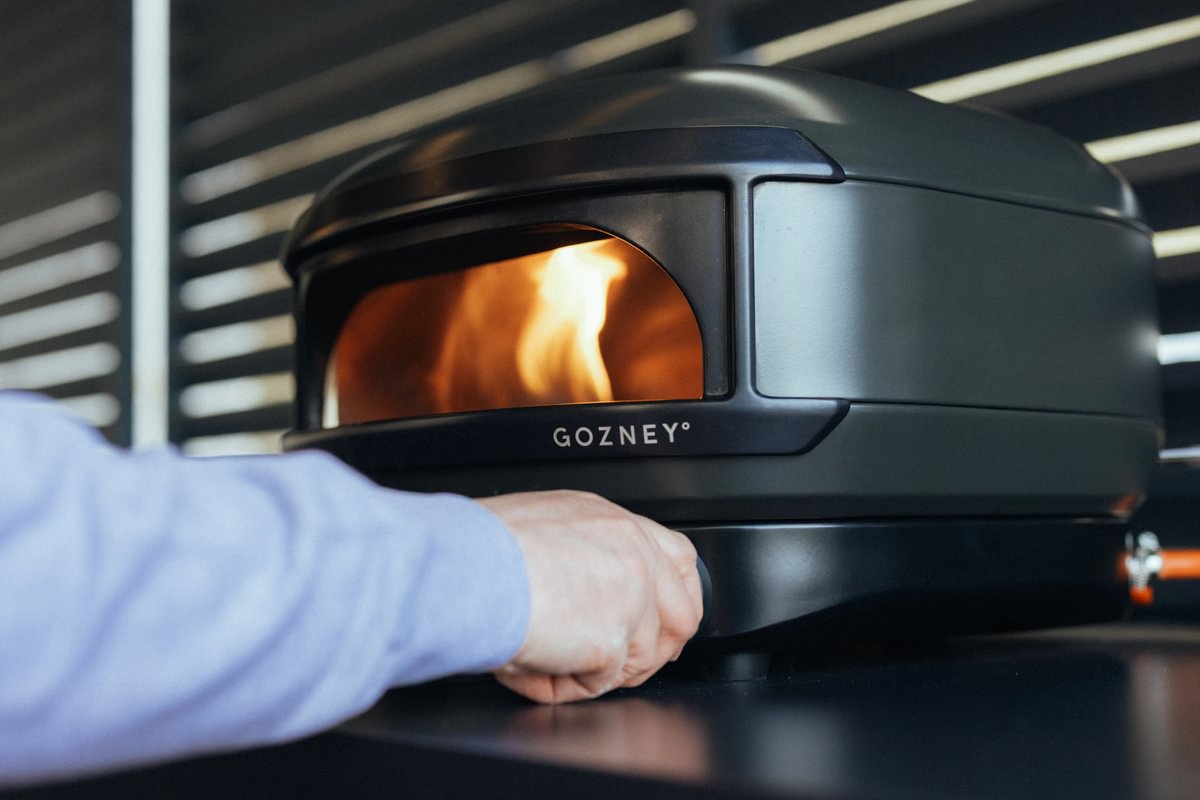 Person interacting with a Gozney pizza oven in a kitchen setting