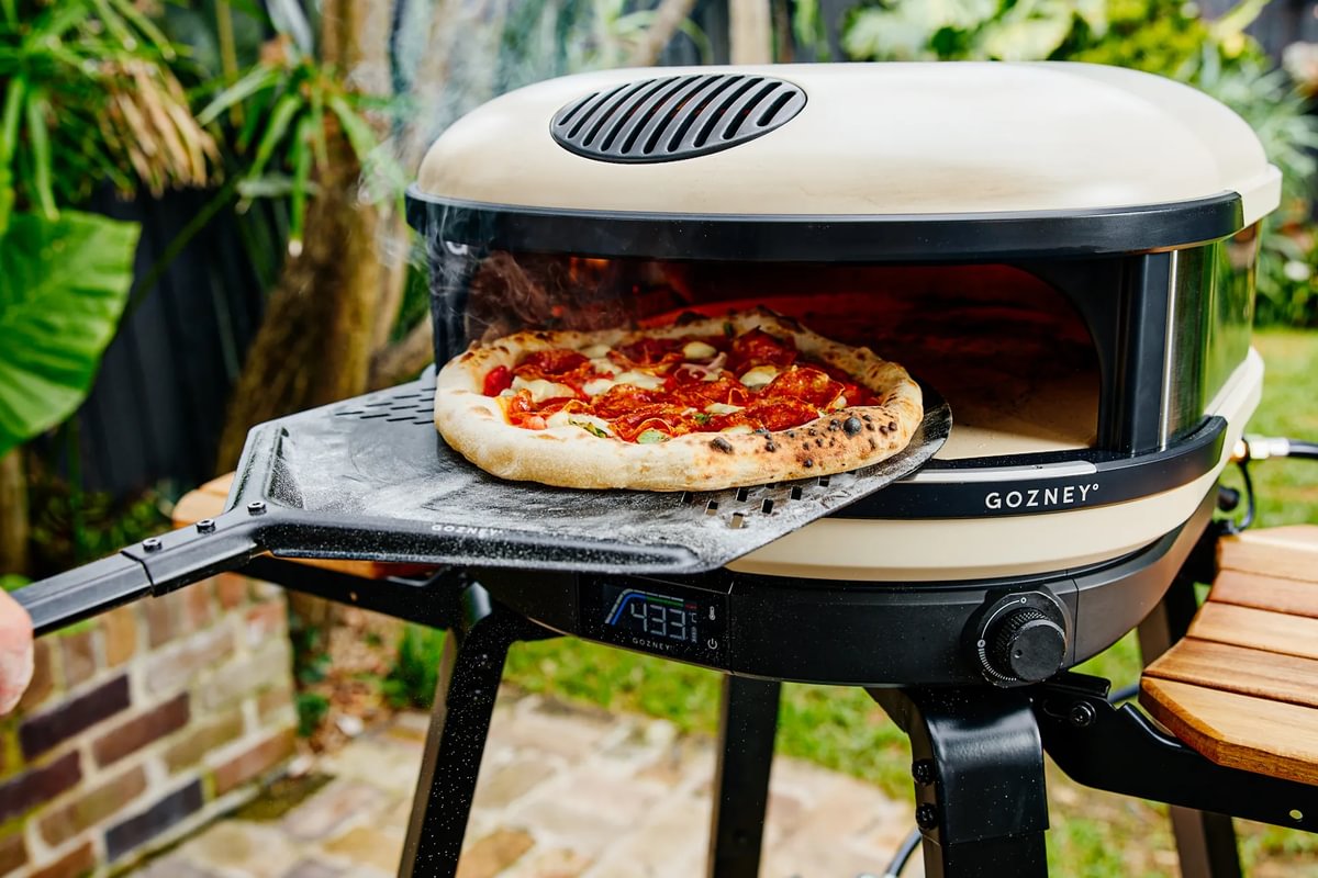 Portable pizza oven with a pizza inside, set outdoors.