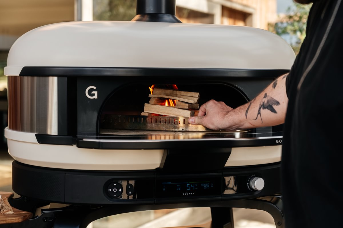 Person putting wood into a wood fire pizza oven