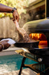 Person grilling a steak on a Gozney Pizza over