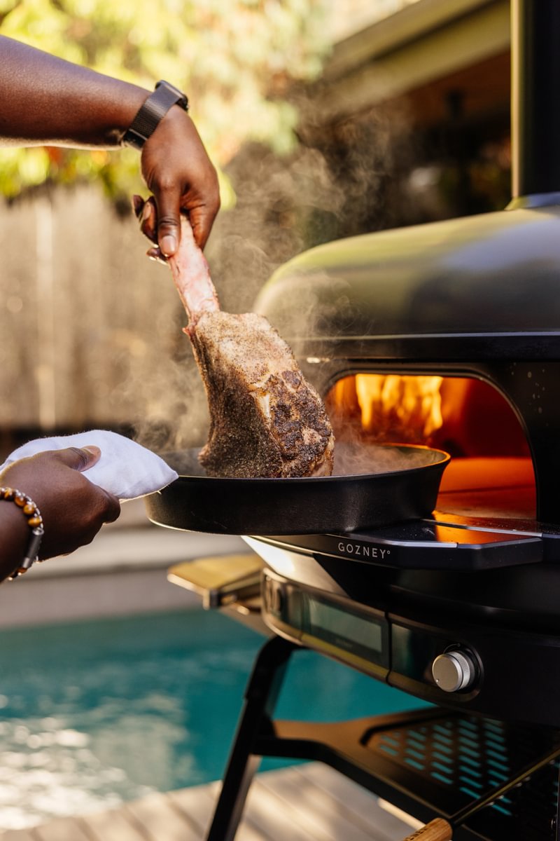 Person grilling a steak on a Gozney Pizza over